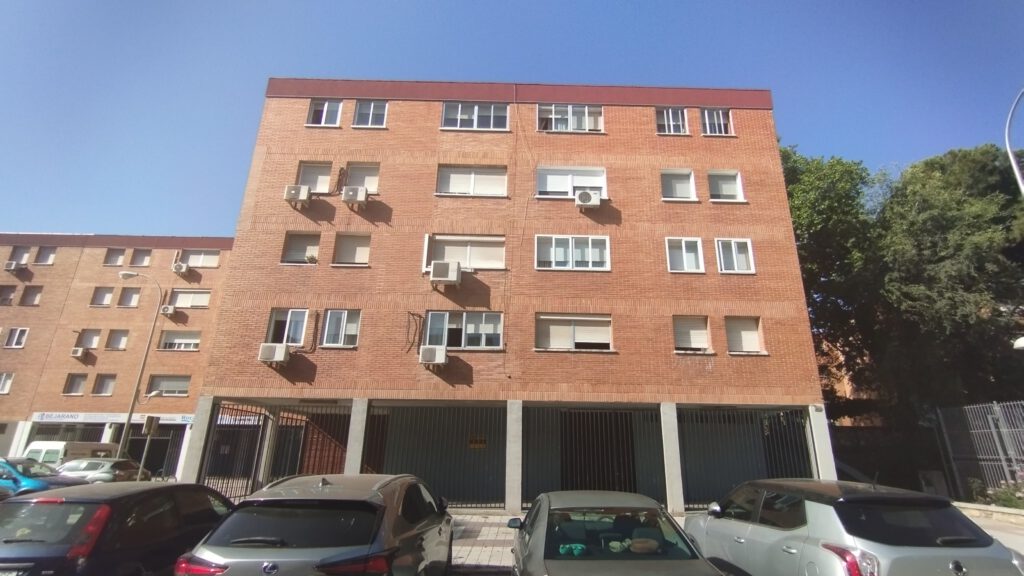 Edificio de apartamentos con coches aparcados enfrente.